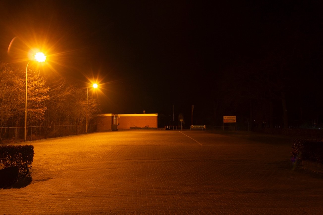 Parkeerplaats naast een sportveld, met lantaarns. Zie bijschrift onder afbeelding